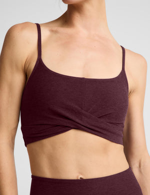 A woman modeling a dark burgundy sports bra and matching high-waisted leggings against a light gray studio background.