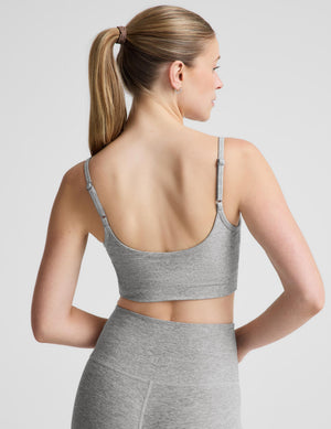 A woman modeling a heather gray sports bra and matching high-waisted leggings against a light gray studio background.