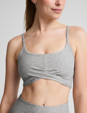 A woman modeling a heather gray sports bra and matching high-waisted leggings against a light gray studio background.