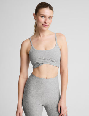 A woman modeling a heather gray sports bra and matching high-waisted leggings against a light gray studio background.