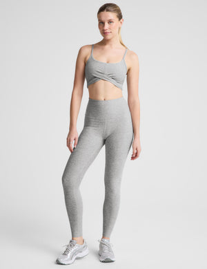 A woman modeling a heather gray sports bra and matching high-waisted leggings against a light gray studio background.
