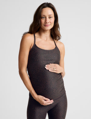 A pregnant woman wearing a dark brown and black leopard-print maternity tank top and matching leggings, standing against a light gray studio background.