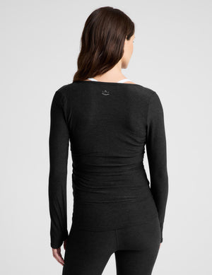 A pregnant woman wearing a black long-sleeve maternity top and matching leggings, standing against a light gray studio background.