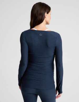 A woman shown from the back wearing a dark navy long-sleeve athletic top and matching leggings against a light gray studio background.