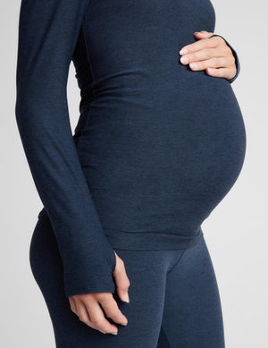 A close-up of a pregnant model wearing a dark navy blue long-sleeve maternity top and matching leggings against a light gray background.