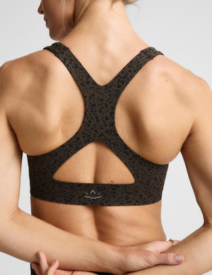A woman modeling a matching dark brown and black leopard-print activewear set, featuring a sports bra and shorts, against a light gray studio background.