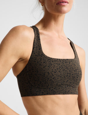 A woman modeling a matching dark brown and black leopard-print activewear set, featuring a sports bra and shorts, against a light gray studio background.