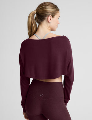 A woman modeling a dark burgundy long-sleeve crop top and matching high-waisted leggings against a light gray studio background.