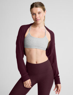A woman modeling a dark burgundy long-sleeve crop top and matching high-waisted leggings against a light gray studio background.