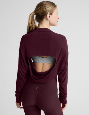 A woman modeling a dark burgundy long-sleeve crop top and matching high-waisted leggings against a light gray studio background.