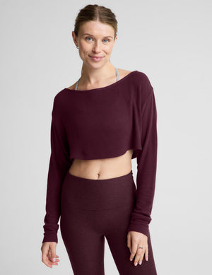 A woman modeling a dark burgundy long-sleeve crop top and matching high-waisted leggings against a light gray studio background.