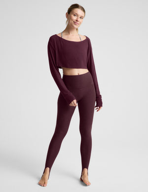 A woman modeling a dark burgundy long-sleeve crop top and matching high-waisted leggings against a light gray studio background.
