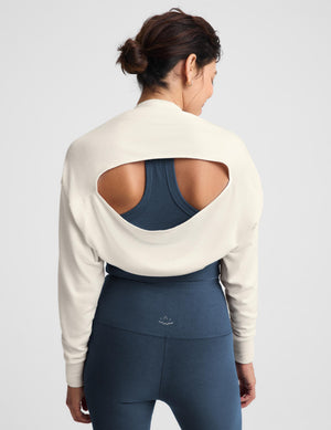 A woman modeling a matching activewear set consisting of a cream off-the-shoulder long-sleeve crop top and high-waisted navy blue leggings, paired with white sneakers, against a light gray studio background.