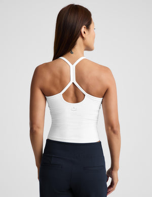 A woman wearing a white crop tank and dark navy bottoms, photographed against a light gray studio background.