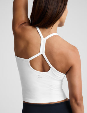 A woman wearing a white crop tank and dark navy bottoms, photographed against a light gray studio background.