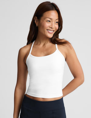 A smiling woman wearing a white crop top and dark navy bottoms, photographed against a light gray studio background.