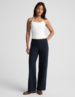 A woman wearing a white crop tank and dark navy bottoms, photographed against a light gray studio background.