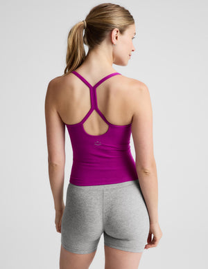 A woman wearing a bright magenta-pink ribbed tank top and heather gray leggings, standing against a light gray studio background.