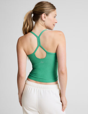A woman modeling a green ribbed tank top with white sweatpants against a light gray studio background.