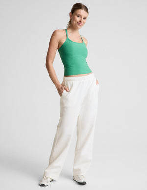 A woman modeling a green ribbed tank top with white sweatpants against a light gray studio background.