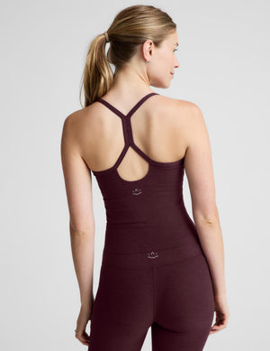 A woman modeling a dark plum-colored athletic tank top and matching leggings against a light gray studio background.