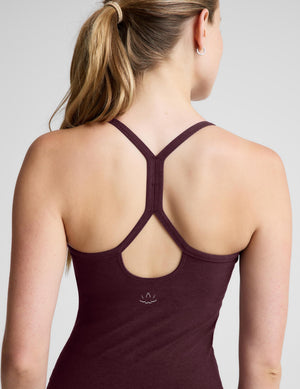 A woman modeling a dark plum-colored athletic tank top and matching leggings against a light gray studio background.