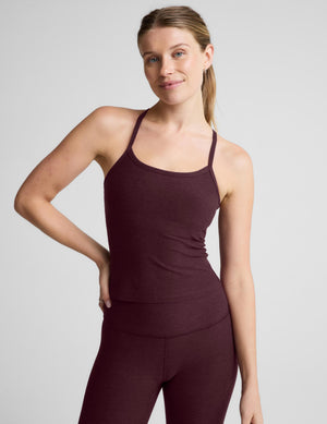 A woman modeling a dark plum-colored athletic tank top and matching leggings against a light gray studio background.