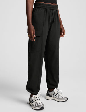 model wearing a black t-shirt and black cargo style pants on a white background. 