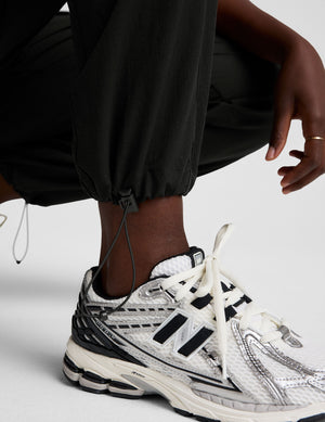 model wearing a black t-shirt and black cargo style pants on a white background. 