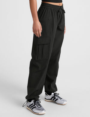Side profile of woman wearing Java Peak Pant™ with cargo pockets, paired with a black crop top and silver sneakers.
