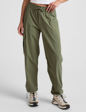 Olive green Peak Pant on model featuring an elastic drawstring waistband, relaxed legs, and side cargo zipper pockets.