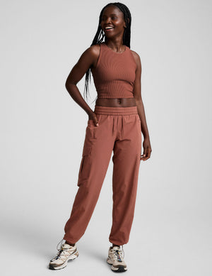 A smiling woman wearing the brown Peak Pant, a relaxed cargo jogger with an elastic waist and side utility pockets.