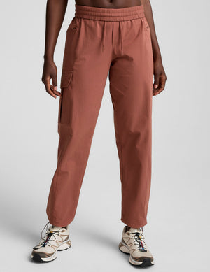Front view of brown Peak Pant with an elastic drawstring waist and cargo pockets, styled with hiking shoes in a studio.