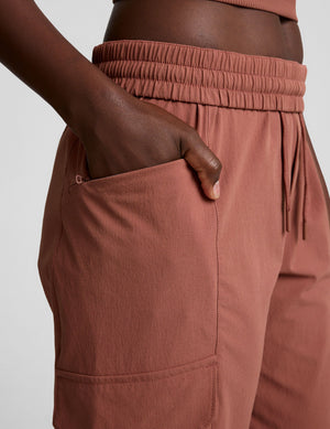 Side close-up of the brown Peak Pant featuring a gathered elastic waistband, drawcord, and zippered side cargo pocket.