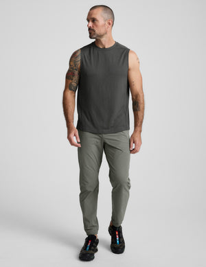 Man wearing a sleeveless dark gray shirt and green joggers on a light gray background. 