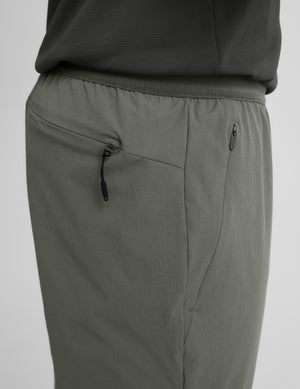 Close-up of green joggers with a back and side zipper on a light gray background. 