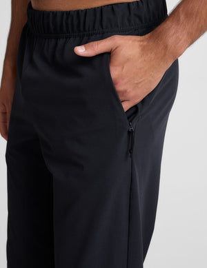 man wearing a gray crew neck t-shirt and blue joggers on a plain background. 