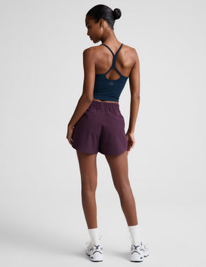 Woman wearing a navy tank top and purple shorts on a plain background. 