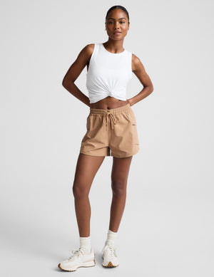 Woman wearing a white tank top and beige shorts on a plain background. 