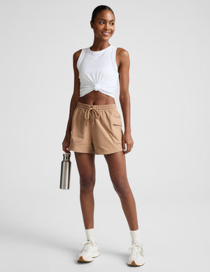 Woman wearing a white tank top and beige shorts on a plain background. 