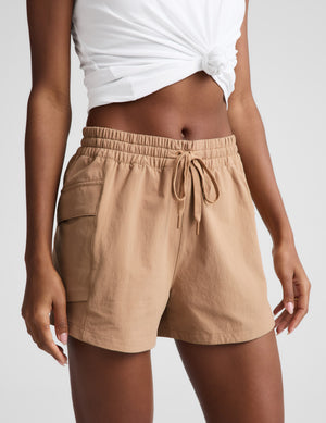 Woman wearing a white tank top and beige shorts on a plain background. 