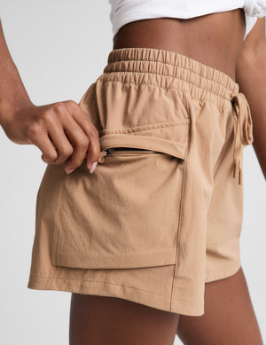 Woman wearing a white tank top and beige shorts on a plain background. 