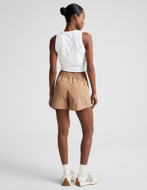 Woman wearing a white tank top and beige shorts on a plain background. 