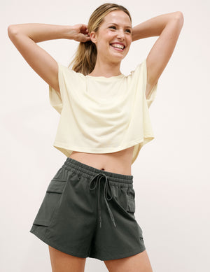 Woman wearing a yellow crop top and green shorts on a light background. 