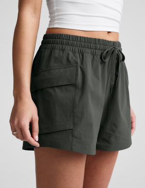 Person wearing dark green shorts with a white top on a light gray background. 