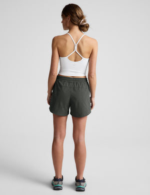 Woman wearing a white tank top and green shorts on a plain background. 