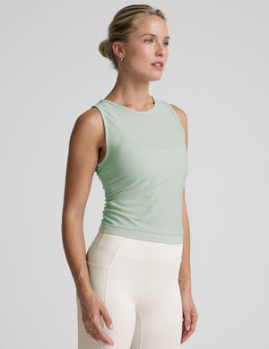 model wearing a blue sleeveless top and white pants on a plain background.