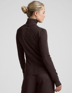 woman wearing a brown turtleneck and pants on a light gray background. 