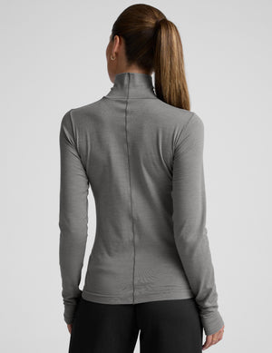 model wearing a gray turtleneck and black pants against a plain background. 
