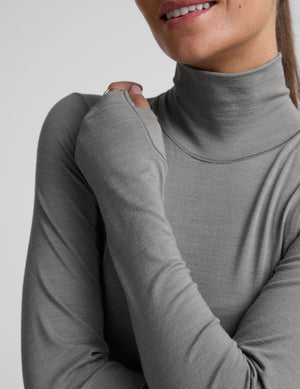 model wearing a gray turtleneck and black pants against a plain background. 